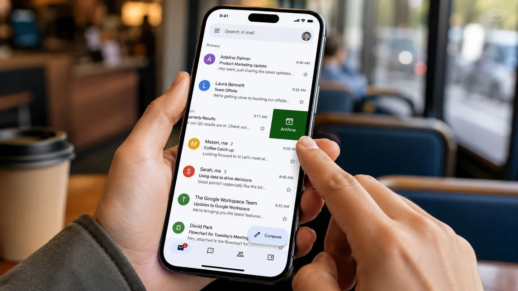 A person swiping an email to archive it on their smartphone screen while in a cafe.