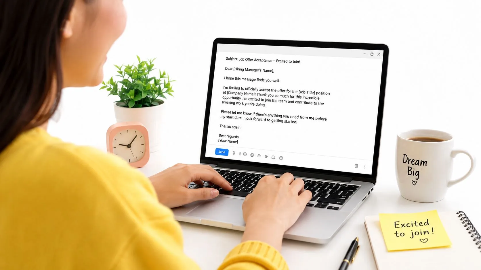 Una persona che indossa un maglione giallo mentre scrive un'email di accettazione di un'offerta di lavoro su un computer portatile.