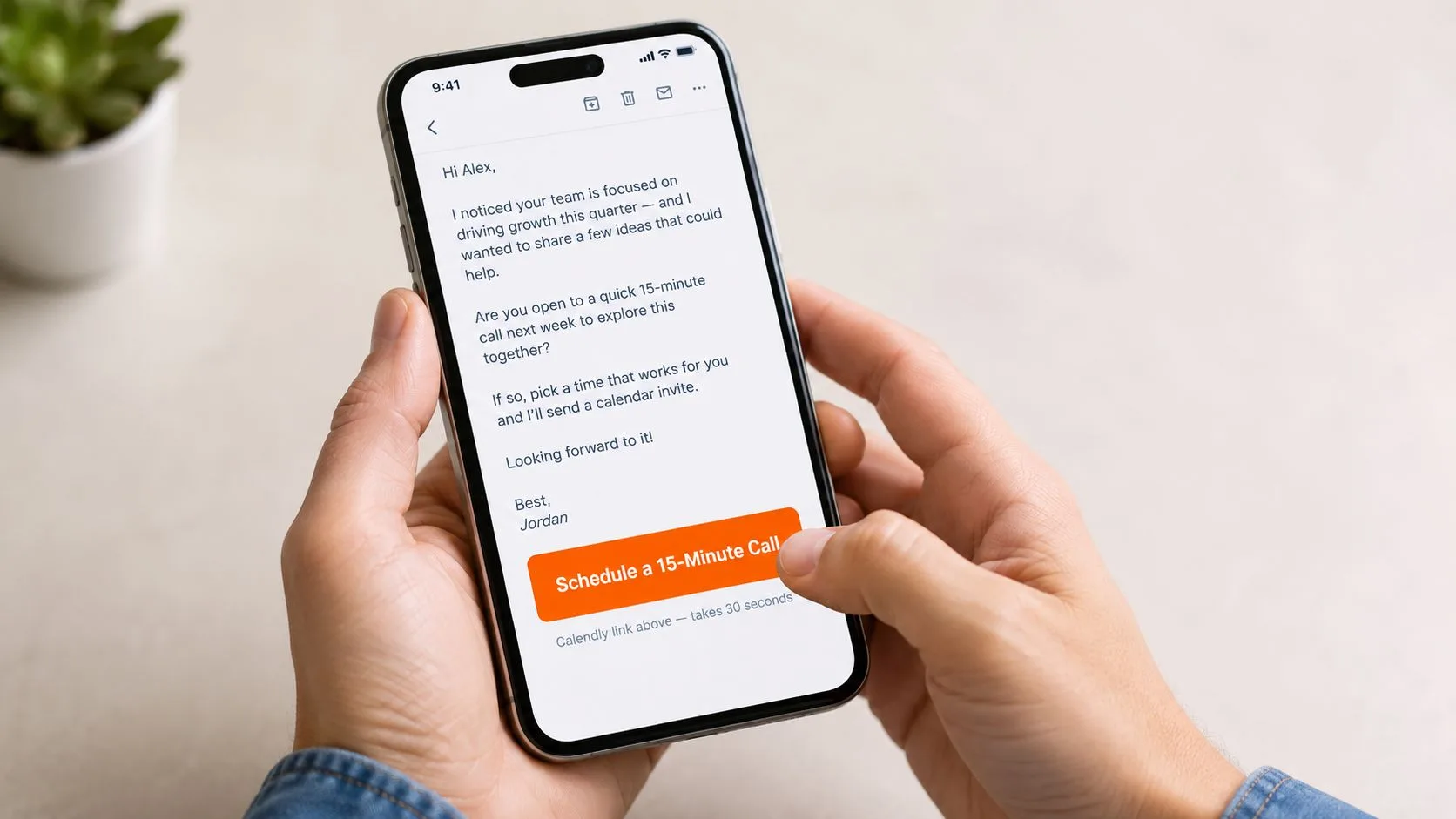 A person holding a smartphone displaying an email with a orange schedule a call button.